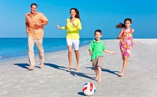 Parents with children kick a ball on the beach.