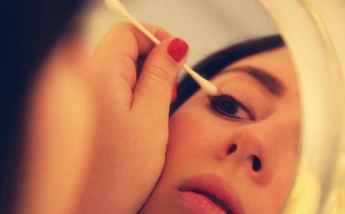 The girl looks in the mirror and puts oil on her eyelids