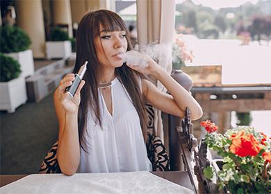 The girl in the cafe smokes an electronic cigarette