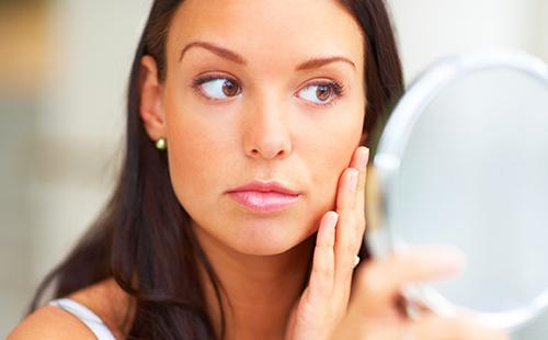 The brown-eyed girl strictly examines her cheeks in the mirror.