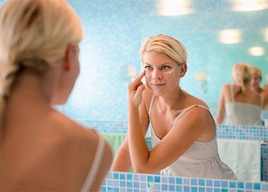 Woman applies cream on face.
