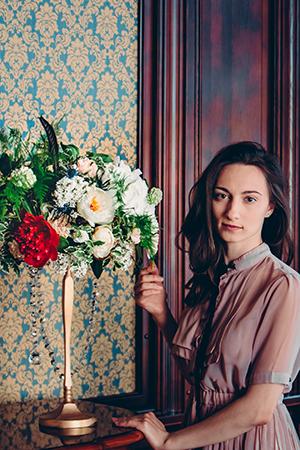 Natalya leans on a table with a bouquet
