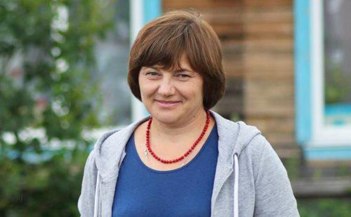 Maria stands in the background of her house