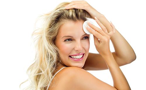 Beautiful blonde rubs her forehead with a cotton pad