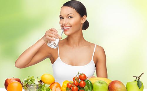 Woman in a white top with a glass of water and fruit
