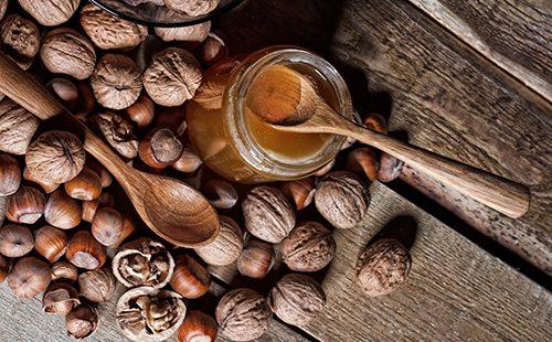 Jar of honey and different nuts on a wooden table