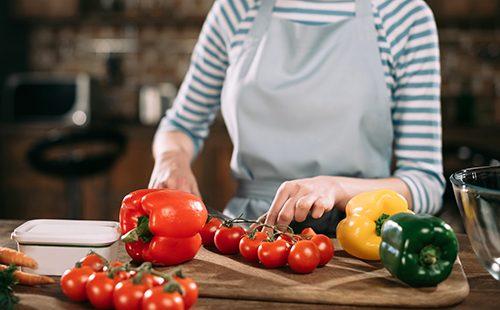 Woman cuts tomatoes and peppers into a salad