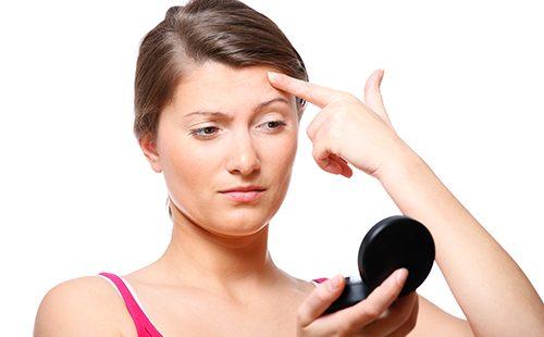 Woman examines pimple in the mirror