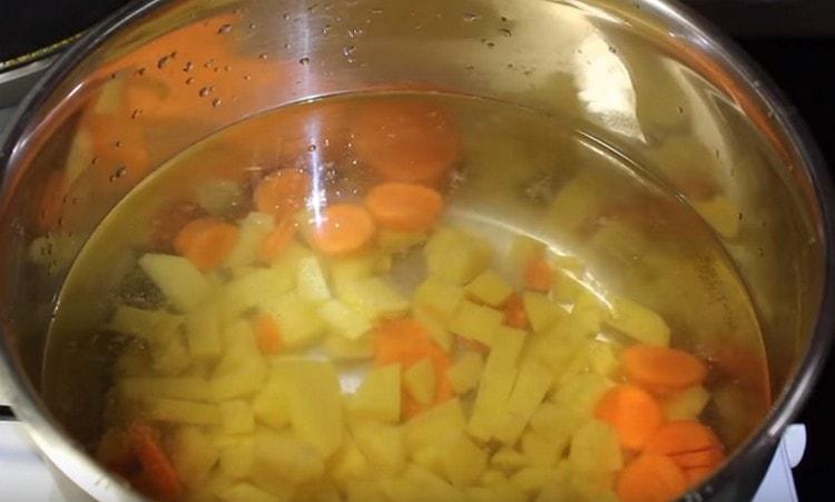 Pour water into a pan and add potatoes and carrots to it.