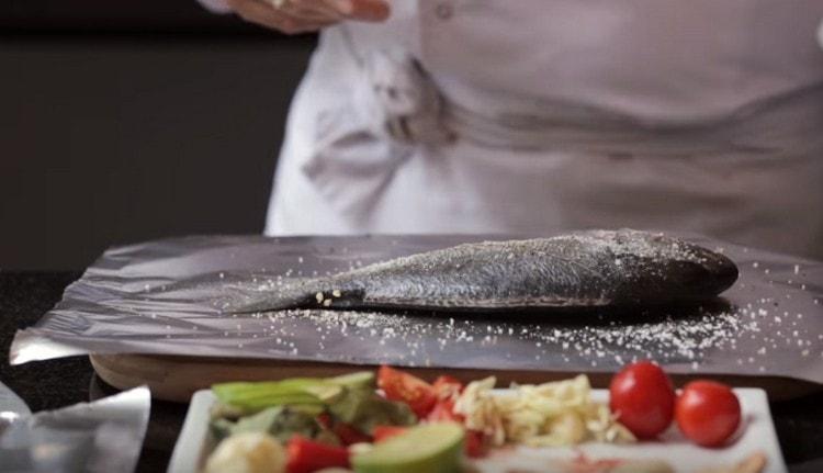 Having made an incision on the fish, salt and pepper it.