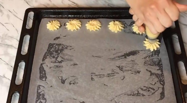 Using a pastry bag with a nozzle, we place cookies on parchment.