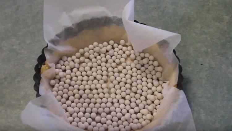 We cover the dough in the form with a piece of parchment and pour beans, rice or other cargo, we send it to the oven,