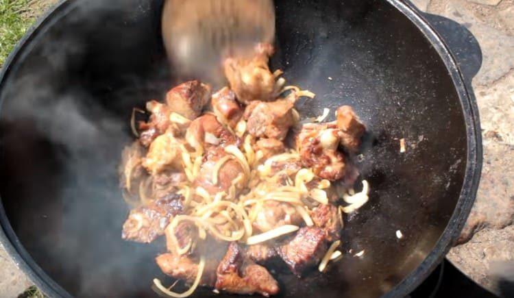 We return the lamb to the cauldron, add the onion and fry.