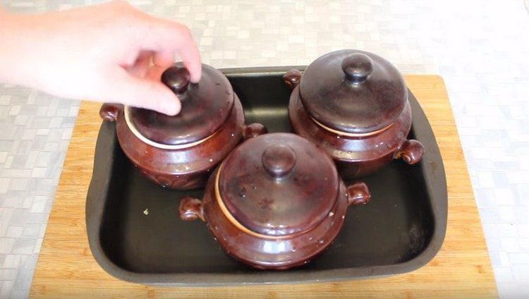 We cover the pots with lids, put on a baking sheet and put in the oven.